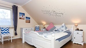 A bedroom with a white bed, a nightstand, a dresser, and a window with curtains. - Ferienwohnung Haus Heimathafen (Esens)