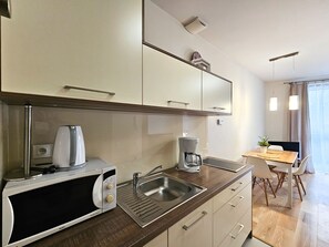Una cocina moderna con microondas integrado, cafetera y lavaplatos. Hay un comedor con una mesa y sillas.