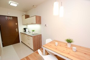 A modern kitchen with wooden cabinets, a sink, and a small potted plant. There is a dining table with chairs and a small white table lamp. - Bałtycka (BA10) - BA10 (Swinoujscie)