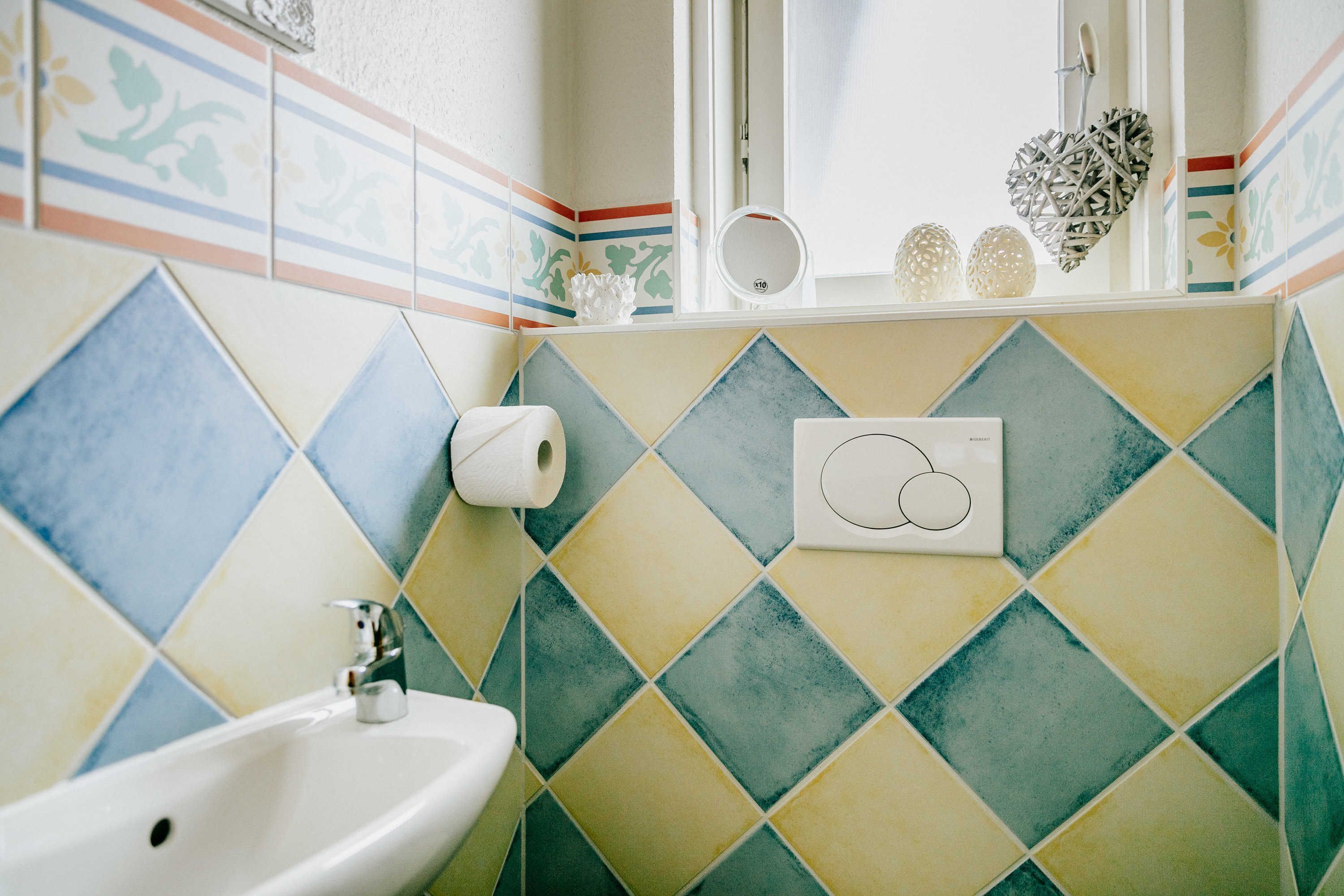 A bathroom with a sink, toilet paper, and decorative items on the wall.
