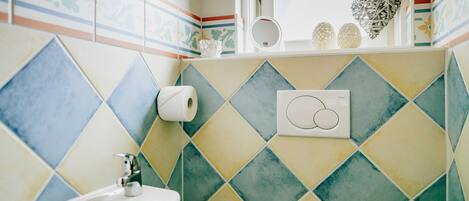 A bathroom with a sink, toilet paper, and decorative items on the wall.