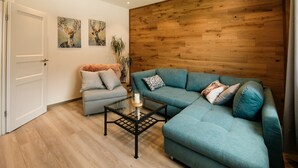 Ein modernes Wohnzimmer mit einem türkisfarbenen Sofa, einem Glastisch und einer Holzwand.