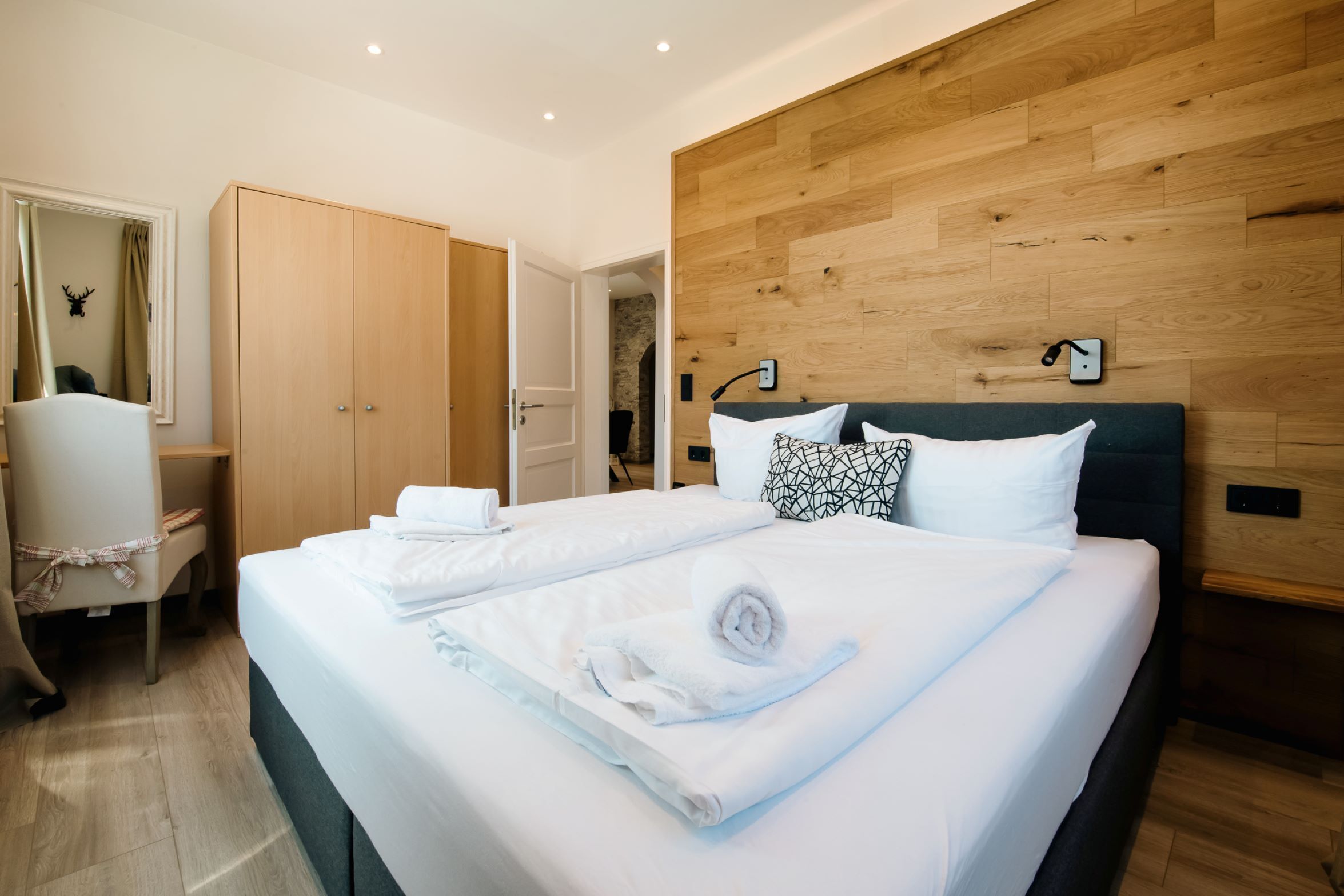 Moderni hotellihuone, jossa on suuri sänky, puinen pääty ja työpöytä tuolilla.