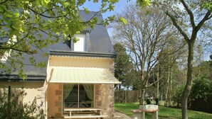 A house with a covered outdoor seating area, a picnic table, and a stone bench.