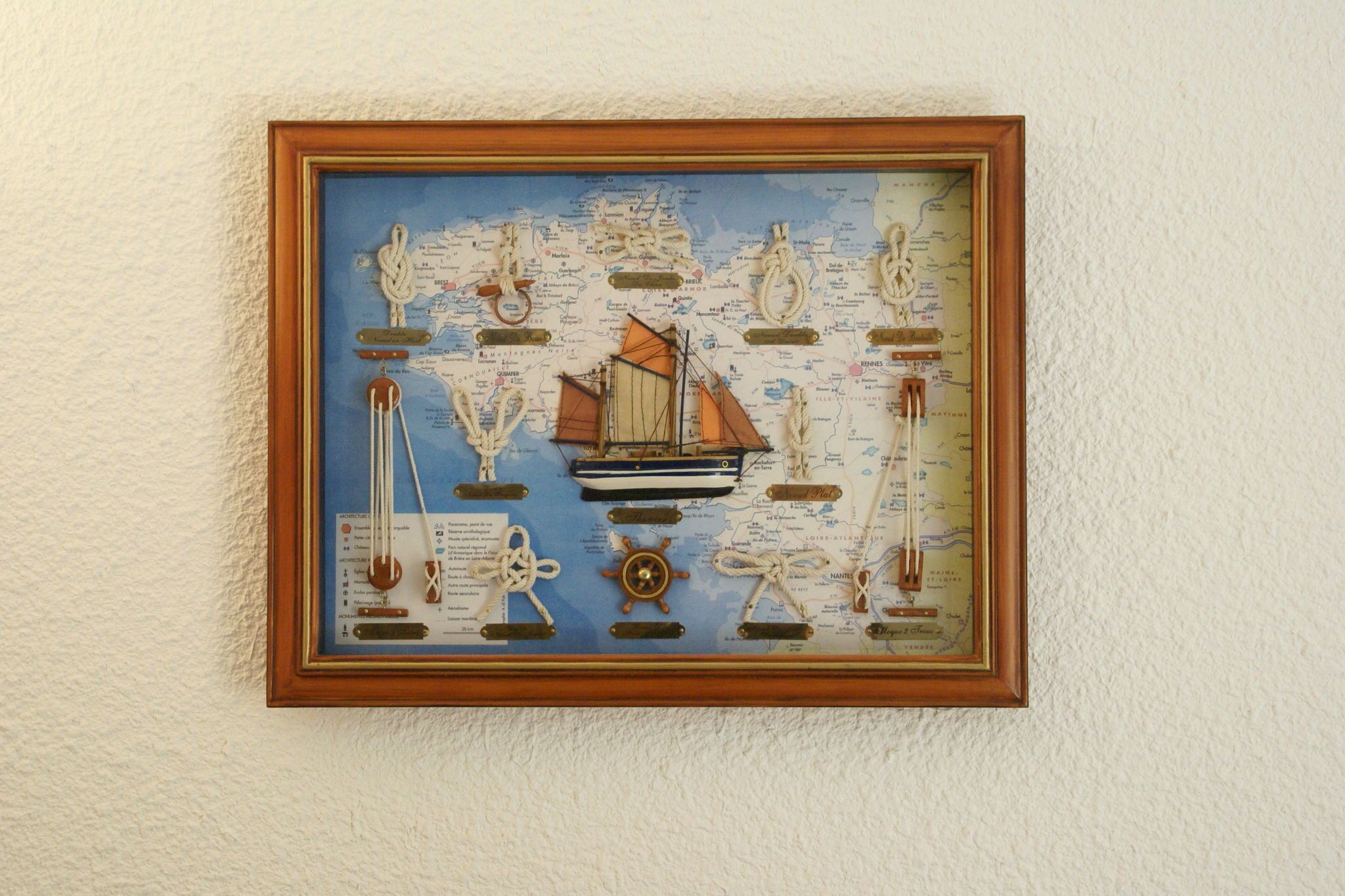 A framed nautical-themed artwork with a ship, anchors, and a compass.