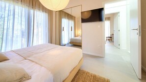 Un dormitorio con una cama grande, un televisor de pantalla plana montado en la pared y vista a un bosque por la ventana.