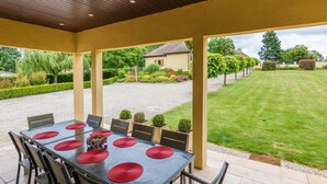 Eine Terrasse im Freien mit einem Essplatz, umgeben von Stühlen, mit Blick auf einen gepflegten Garten und ein Haus im Hintergrund.
