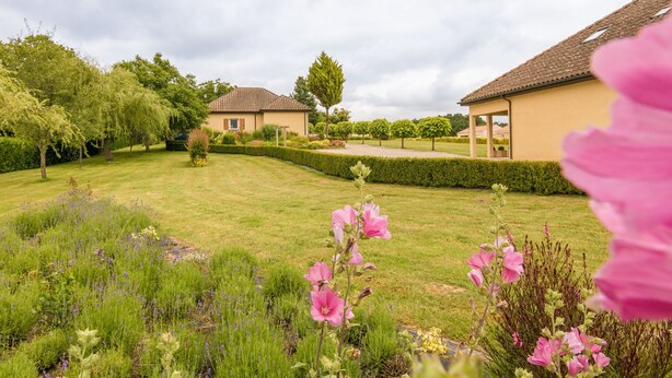 Ein Wohnhaus mit gepflegtem Rasen, einem Garten mit verschiedenen Pflanzen und Blumen sowie einem Gebäude mit Ziegeldach.
