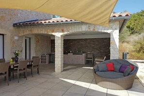 Un patio al aire libre con muros de piedra, una mesa de comedor con sillas, un sofá de mimbre y una zona de bar.