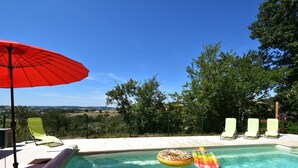 Una piscina con due cerchi gonfiabili, un ombrellone rosso e diversi lettini.
