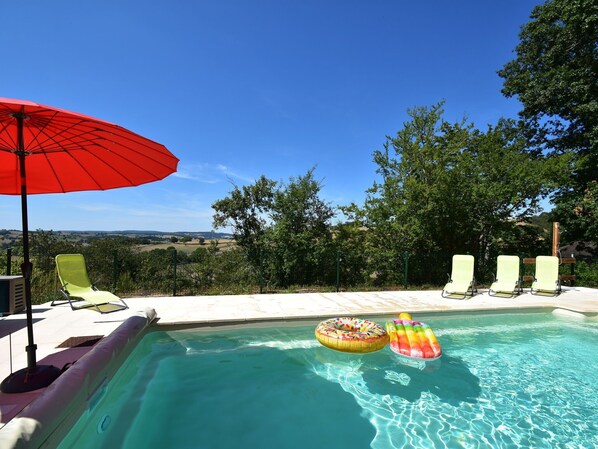 A swimming pool with two inflatable rings, a red umbrella, and several lounge chairs.