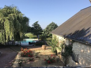Un jardin avec une piscine, un bâtiment en pierre et un saule.