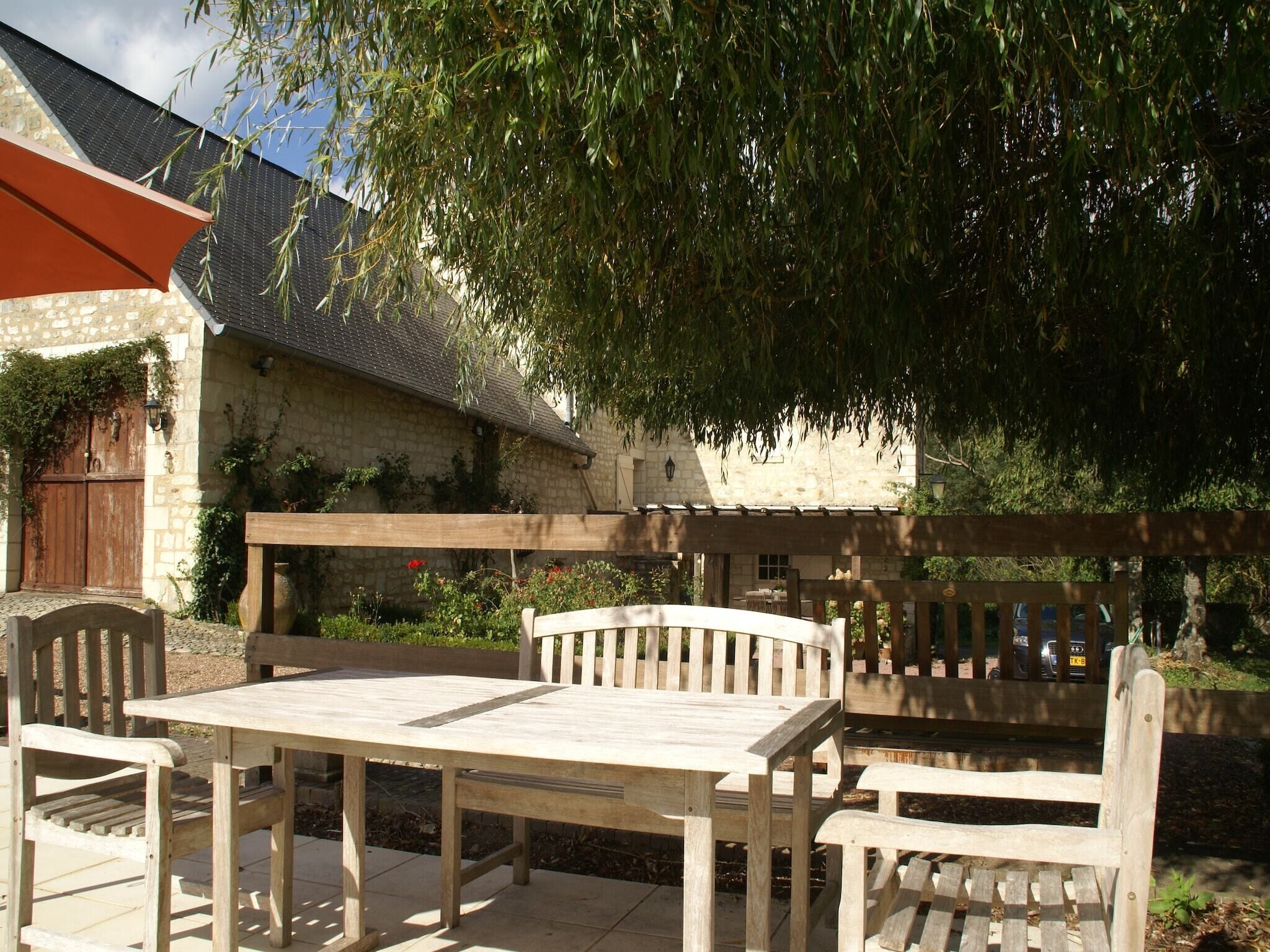 Un conjunto de mesa y sillas de madera al aire libre, con un edificio de piedra al fondo.