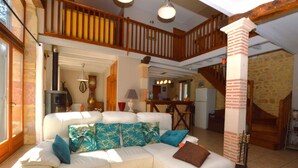A spacious living area with a white sectional sofa, a wooden staircase, and a kitchen in the background. - Family Retreat in Thédirac (Thedirac)