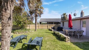 A backyard with two lounge chairs, a covered patio area with a table and chairs, and a red umbrella. - Charming Home with Orchard (Montaigu-La-Brisette)