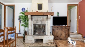 A living room with a stone fireplace, a television, wooden furniture, and a decorative cow figurine. - Charming Home with Orchard (Montaigu-La-Brisette)