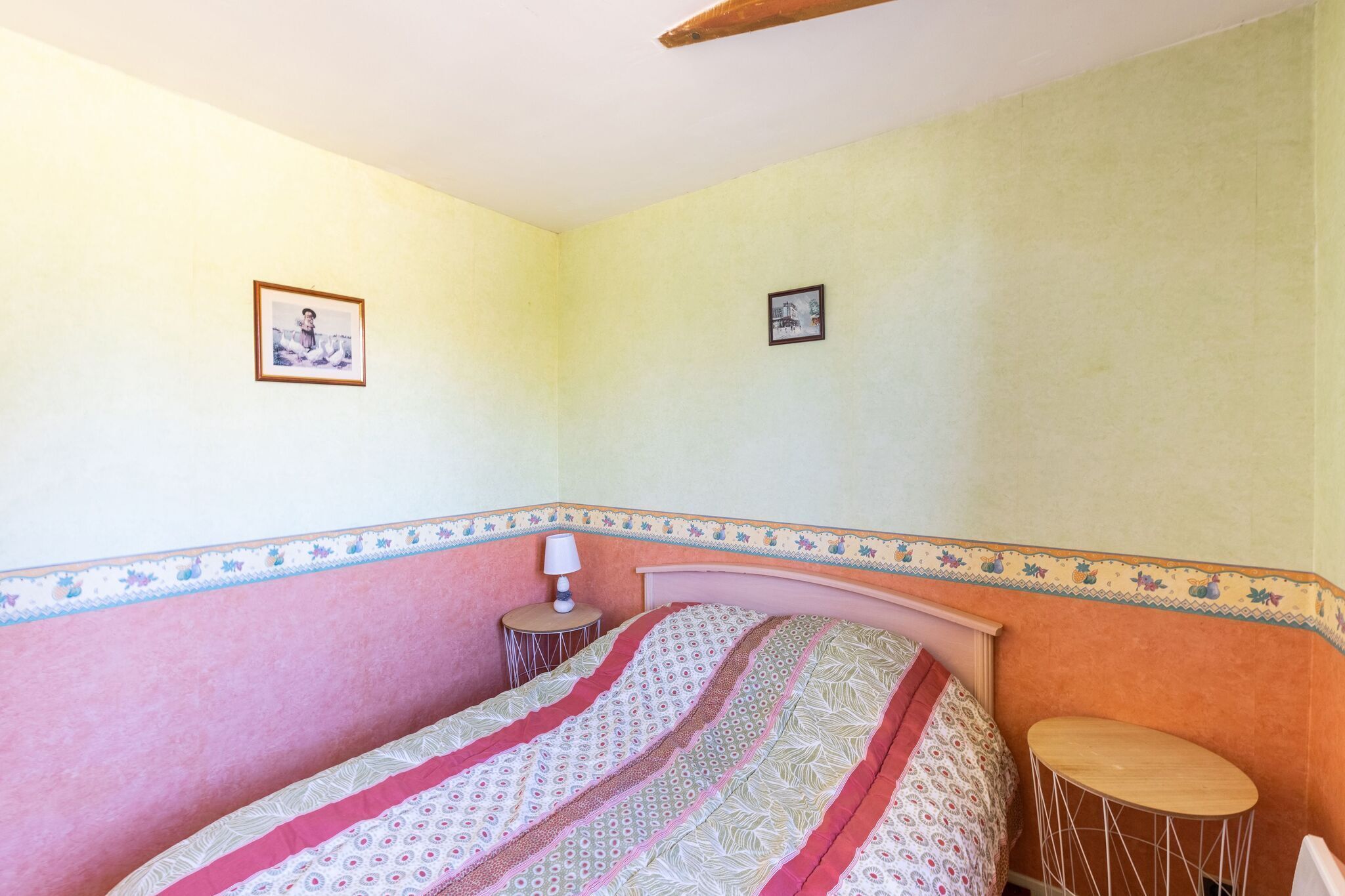 A bedroom with a bed, a bedside table, a lamp, and two framed pictures on the wall.