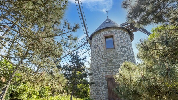 A stone windmill with a wooden door and a window, surrounded by pine trees. - Charming Home with Orchard (Montaigu-La-Brisette)