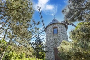 A stone windmill with a wooden door and a window, surrounded by pine trees. - Charming Home with Orchard (Montaigu-La-Brisette)