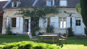 Une maison à deux étages avec un jardin, une table en bois et deux chaises.