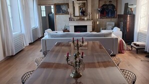 Une salle à manger spacieuse avec une longue table en bois, des canapés blancs recouverts de tissu et un lustre.