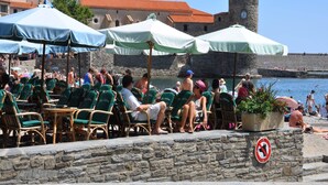 A coastal area with stone walls, outdoor seating, and a historic tower. - Villa in Le Boulou with Scenic Hilltop Views (Le Boulou)