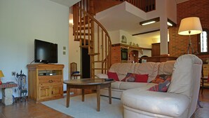 A living room with a sofa, a television on a wooden cabinet, a staircase, and a brick wall. - Villa in Le Boulou with Scenic Hilltop Views (Le Boulou)