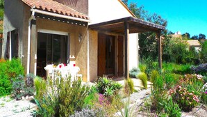 A small house with a tiled roof, a covered porch, and a garden with various plants and flowers. - Villa in Le Boulou with Scenic Hilltop Views (Le Boulou)