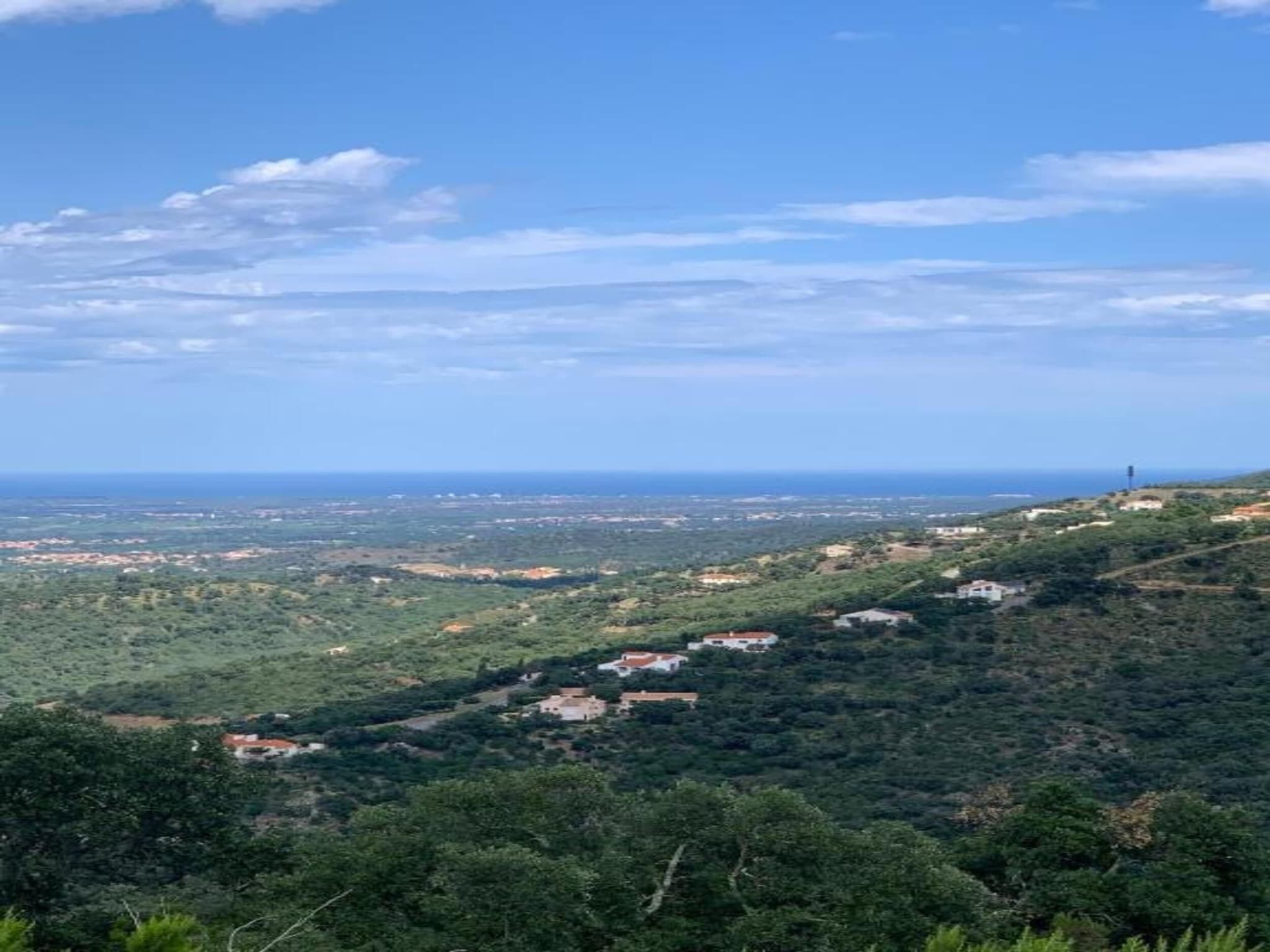 A panoramic view of a hilly landscape with scattered buildings, likely a rural or semi-rural area.