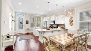 Una cocina amplia con armarios blancos, una mesa de comedor de madera y una lámpara colgante.