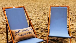 Deux chaises de plage avec des coussins bleus, sur une plage de sable.