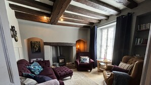 Un salon chaleureux avec une cheminée, des fauteuils confortables et des poutres apparentes.