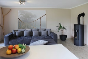 Un salon moderne avec un canapé gris foncé, une grande peinture abstraite, une plante en pot et un poêle à bois noir.