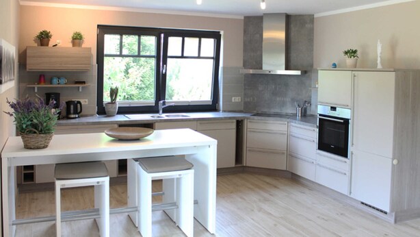 A modern kitchen with white cabinetry, a built-in oven, and a window with a view of greenery. - Ferienwohnung 6 - Ferienhaus Luise Urlaubslust Trassenheide (Trassenheide)