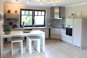 A modern kitchen with white cabinetry, a built-in oven, and a window with a view of greenery.