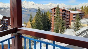 A mountain lodge with multiple balconies, surrounded by snow-covered peaks and evergreen trees. - Arcs 1800, Vogel building, Mont-Blanc view, 200m from slopes and shops (Bourg-Saint-Maurice)