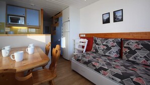 A compact living space with a kitchenette, a dining table with chairs, and a sofa with a patterned cover. - Arcs 1800, Vogel building, Mont-Blanc view, 200m from slopes and shops (Bourg-Saint-Maurice)