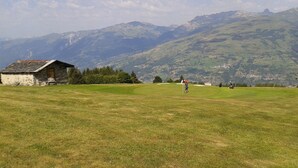 A golf course with a stone building and mountains in the background. - Arcs 1800, Vogel building, Mont-Blanc view, 200m from slopes and shops (Bourg-Saint-Maurice)