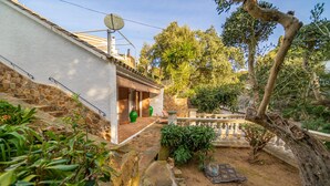 A courtyard with a stone wall, a covered patio area, and a large tree.