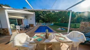 An outdoor patio with a pool, white chairs, and a table set for dining.