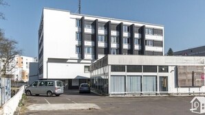 A modern building with a parking lot, a white van, and a smaller adjacent structure.