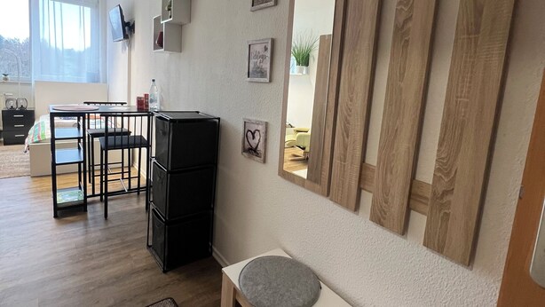 A modern living room with a wooden bench, a TV mounted on the wall, and a large mirror.
