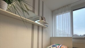 A bedroom with a bed, a potted plant, a window, and a bedside table.