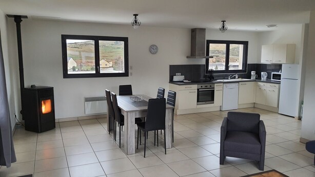 A modern kitchen with a dining area, a wood-burning stove, and large windows offering a view of the countryside.
