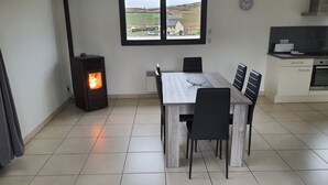 A dining area with a table and chairs, a wood-burning stove, a window with a view, and a kitchen with appliances.
