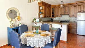 Cozinha com armários de madeira, uma ilha central e uma área de jantar com cadeiras azuis e uma mesa redonda.