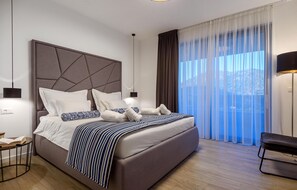 Una camera d'albergo moderna con un grande letto, un comodino, una sedia e un'ampia finestra con tende.