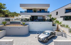 Una moderna casa a due piani con piscina, un'auto parcheggiata davanti e un giardino curato.