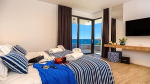 A hotel room with a bed, a TV, a balcony with a view of the sea, and a wooden floor. - Cozy home in Marina with sauna (Marina)
