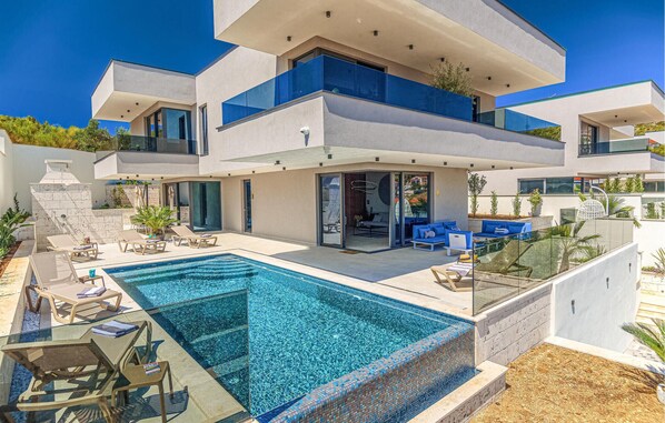 Una casa moderna su due piani con piscina, area salotto esterna e patio coperto.